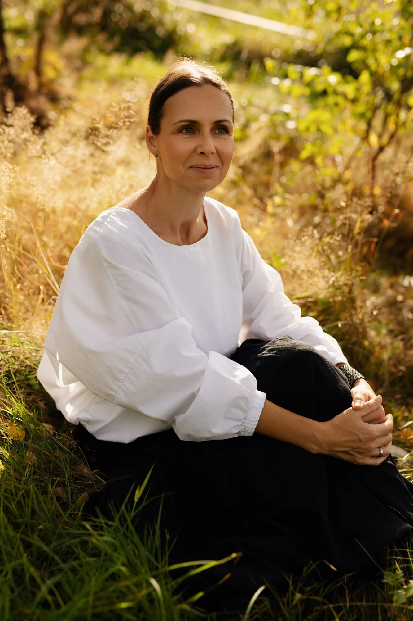 Katarzyna Skupień siedzi w wysokiej trawie, w ciepłym świetle